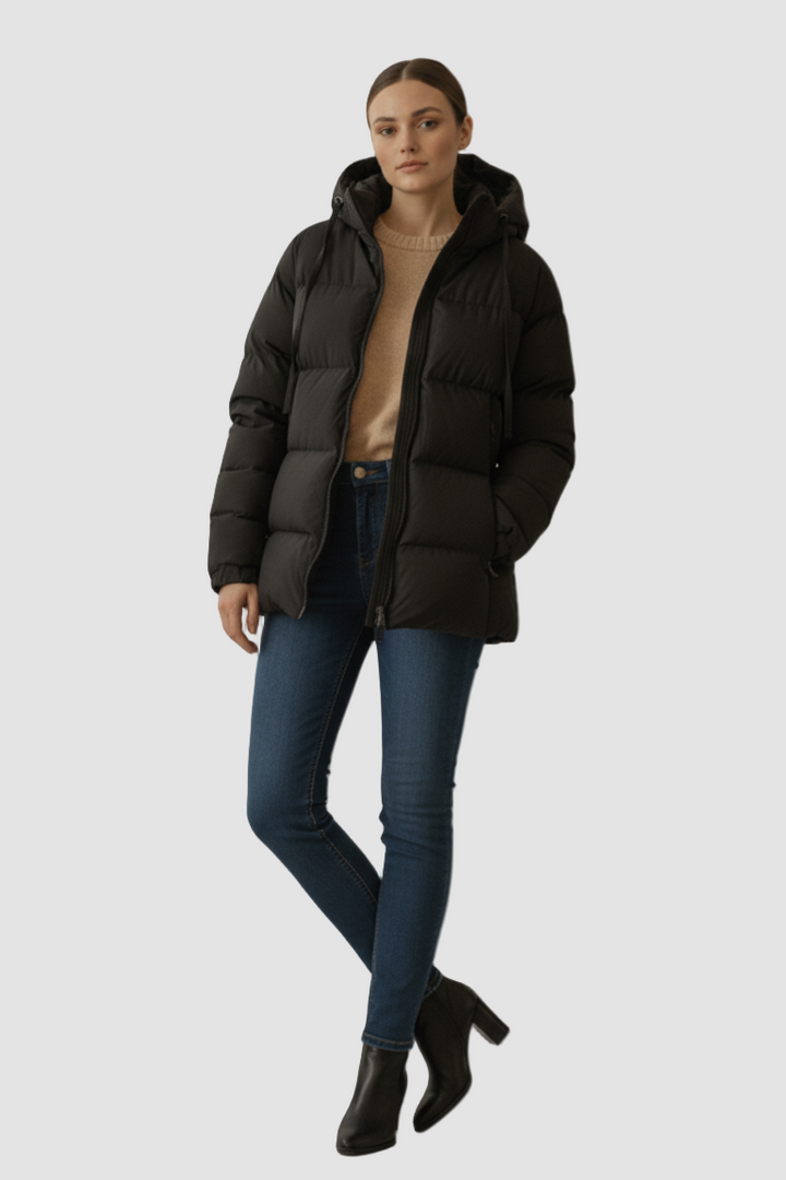 Woman wearing a black puffer jacket, blue jeans, and black boots on a plain background