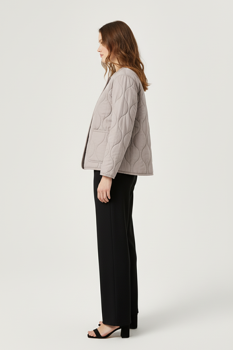 Woman wearing a light gray quilted jacket and black pants on a white background
