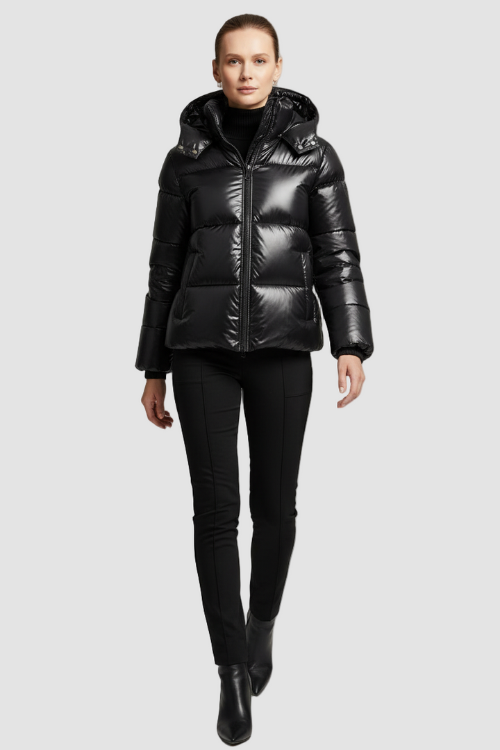 A woman dressed in a black puffer jacket stands against a gray background.