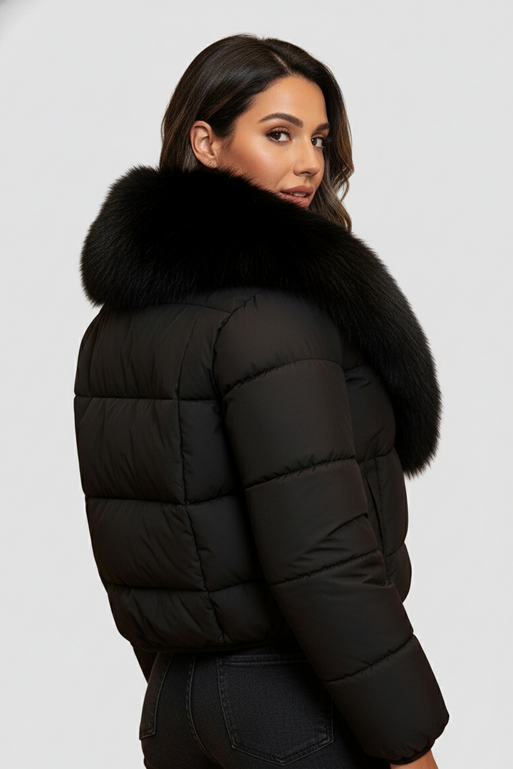 A woman dressed in a black puffer jacket with a fur-lined hood stands against a plain white background.
