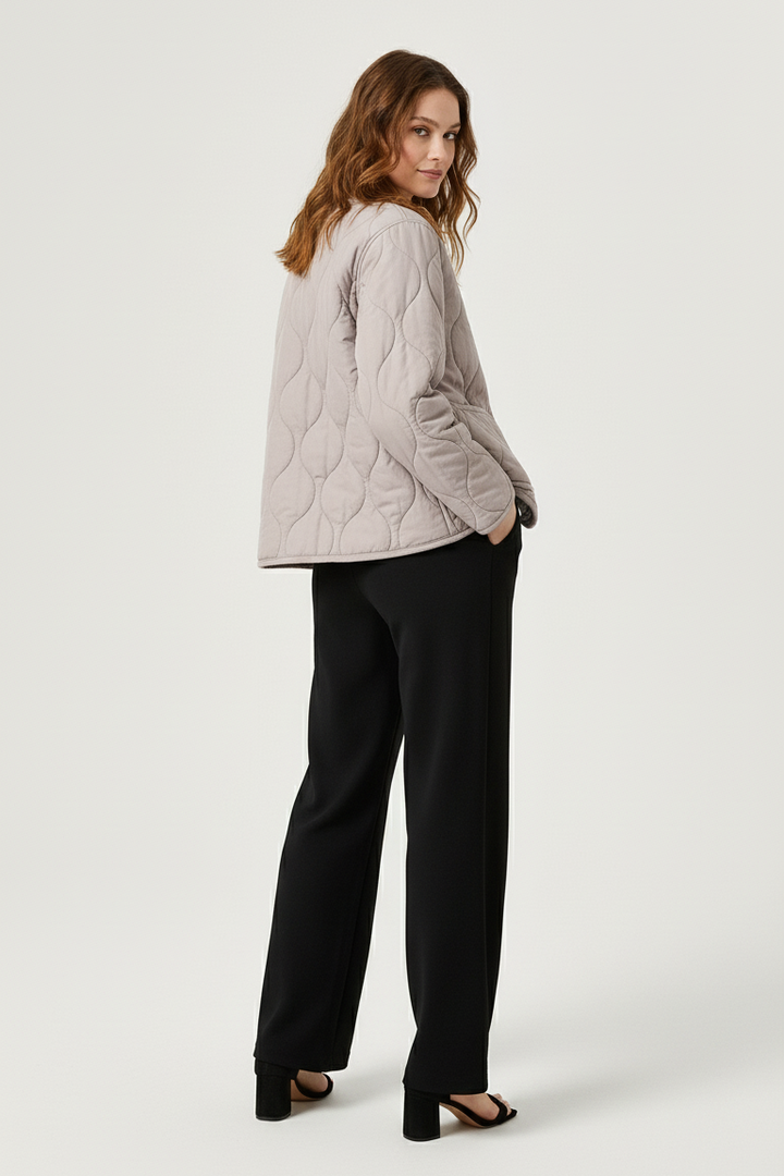 A woman dressed in a light gray quilted jacket and black pants stands against a white background.
