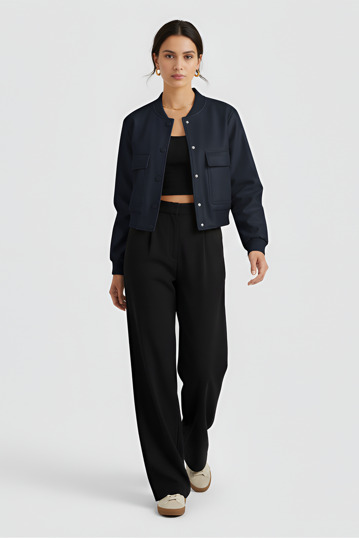 A woman dressed in a navy jacket and black pants stands against a white background.