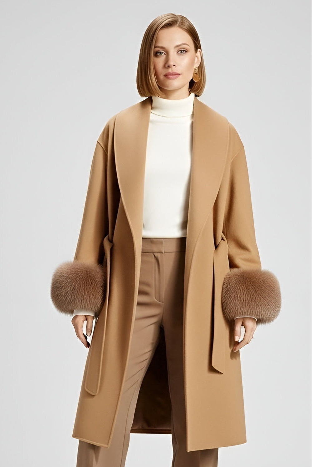 A woman dressed in a tan coat with fur-trimmed cuffs stands against a light gray background.