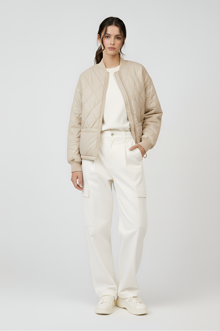 Woman wearing a beige bomber jacket and white pants on a light gray background
