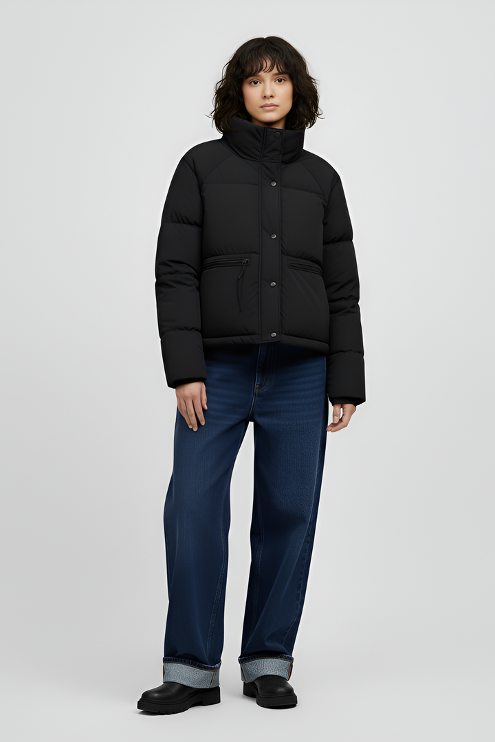 Woman wearing a black jacket, white shirt, and gray pants on a light gray background