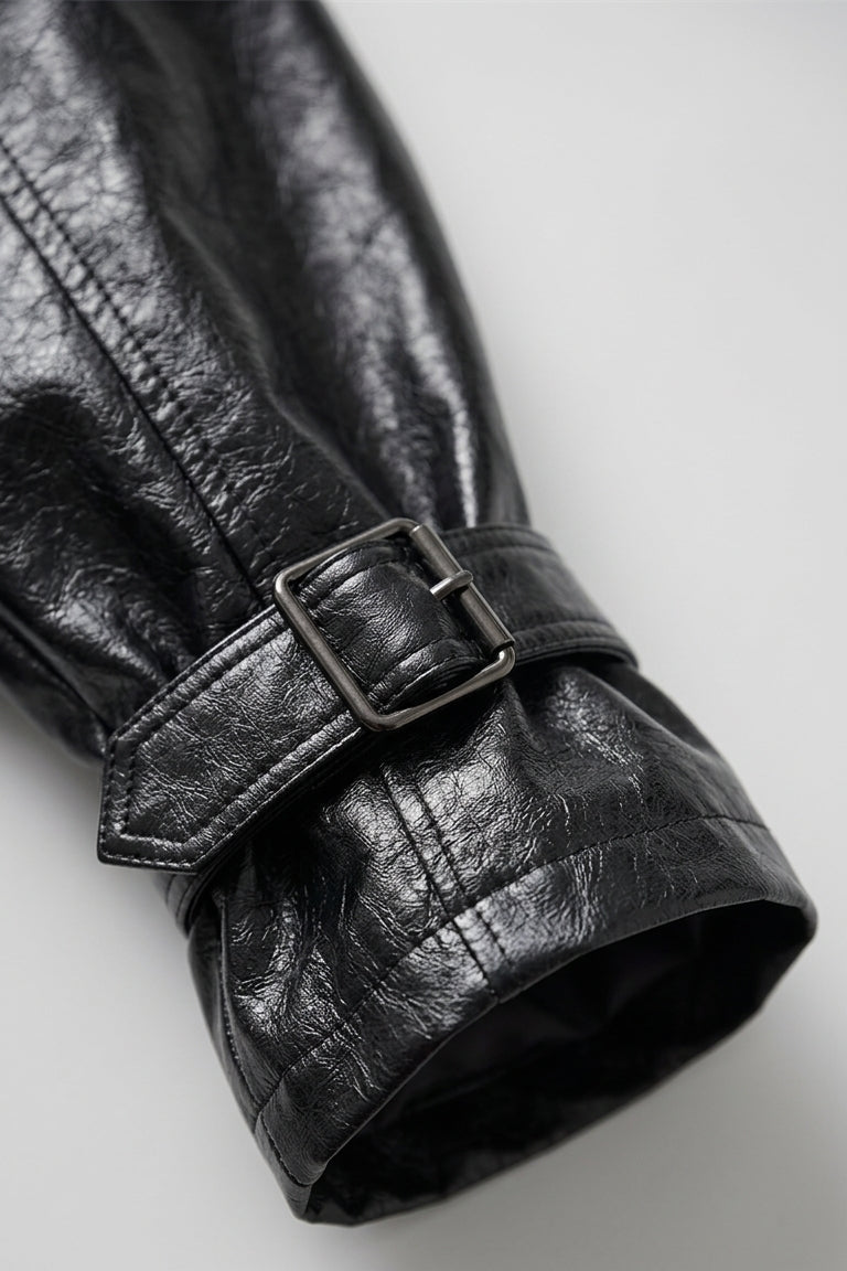 CLAUDINE - Close-up of a black leather trench coat with a belt on a light gray background
