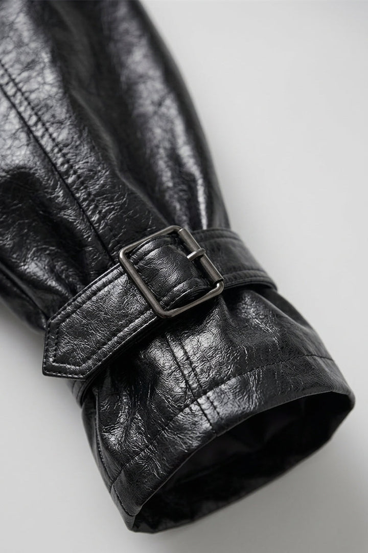 CLAUDINE - Close-up of a black leather trench coat with a belt on a light gray background