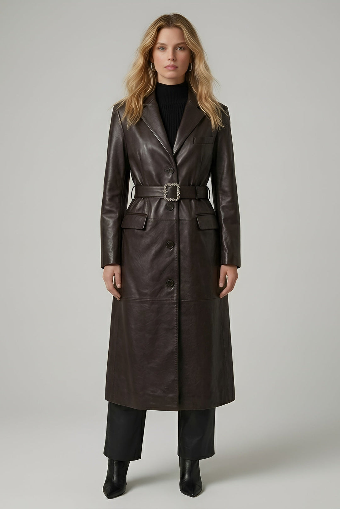 Woman wearing a long brown leather coat on a plain background