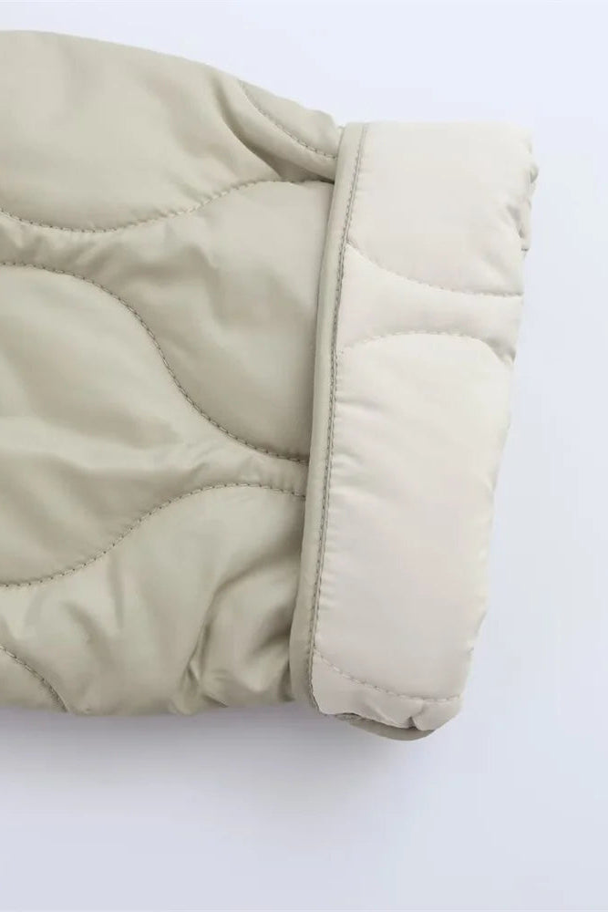 Close-up of a beige quilted jacket on a light gray background