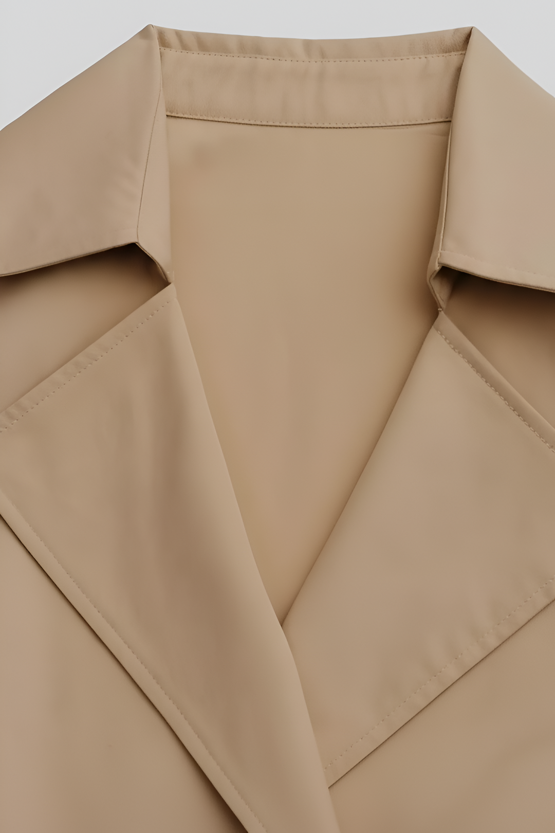 Close-up of a beige trench coat collar on a light gray background