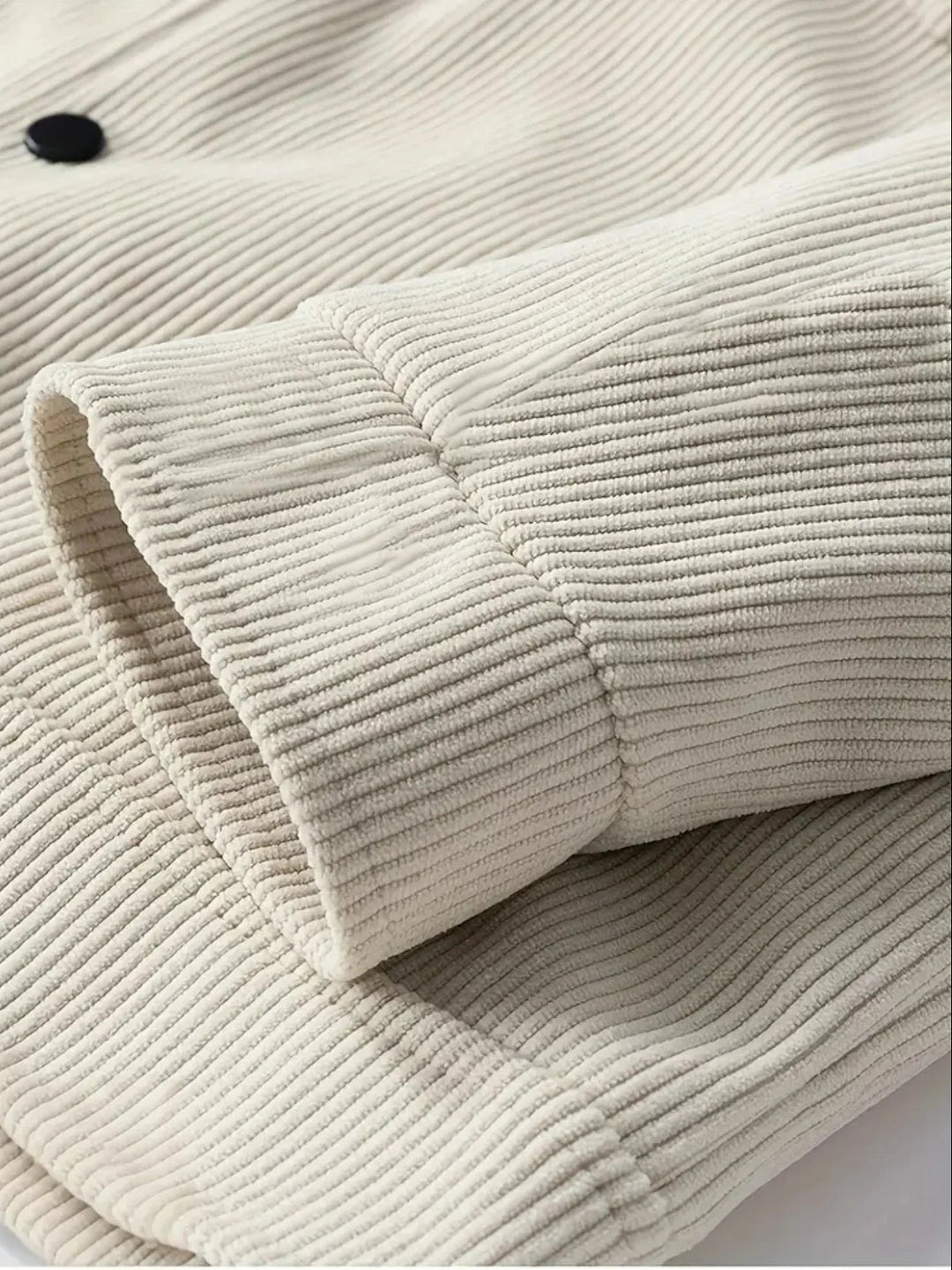 Close-up of beige corduroy fabric with a button on a white background