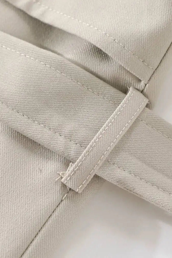 Close-up of beige fabric with a strap and button detail on a white background