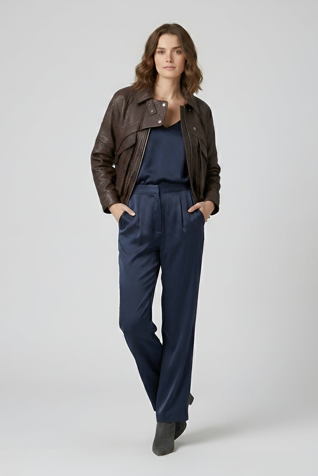 DREW - Woman wearing a brown leather jacket and navy jumpsuit on a white background