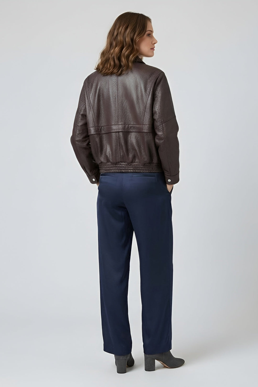 DREW - Woman wearing a brown leather jacket and navy pants on a white background