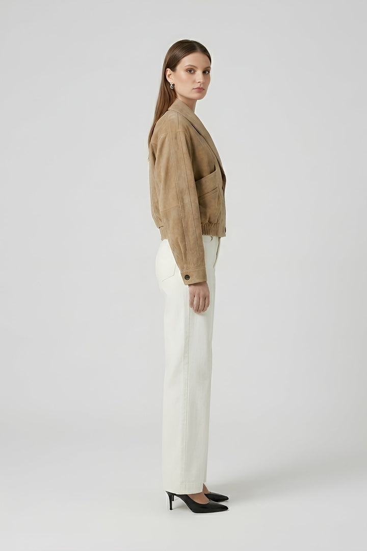 ELISE - Woman wearing a beige jacket and white pants side profile on a plain background