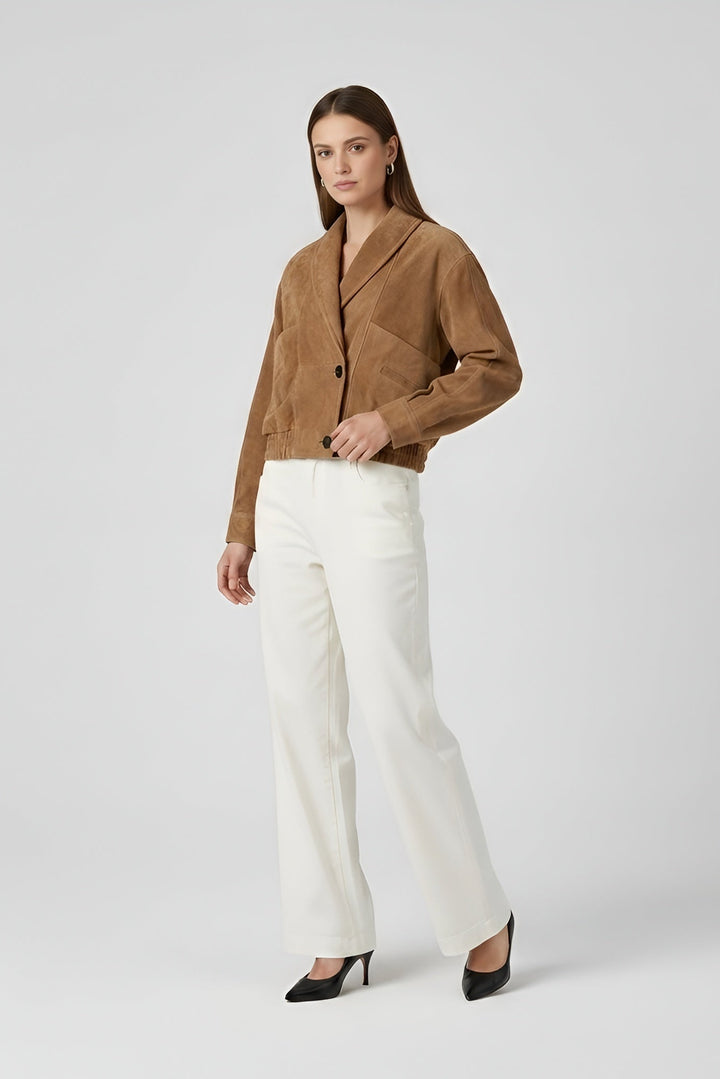 ELISE - Woman wearing a brown jacket and white pants on a plain background