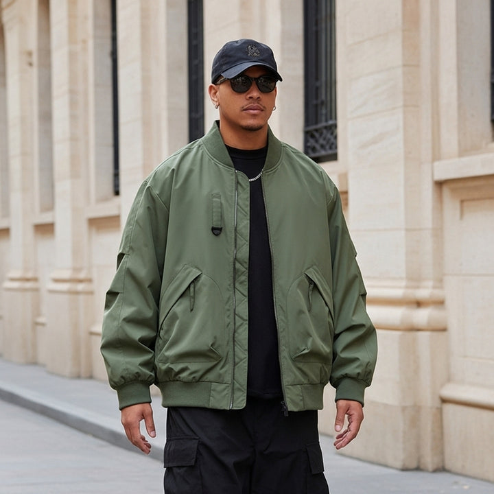 Man wearing a green bomber jacket and black cap standing in front of a beige building.