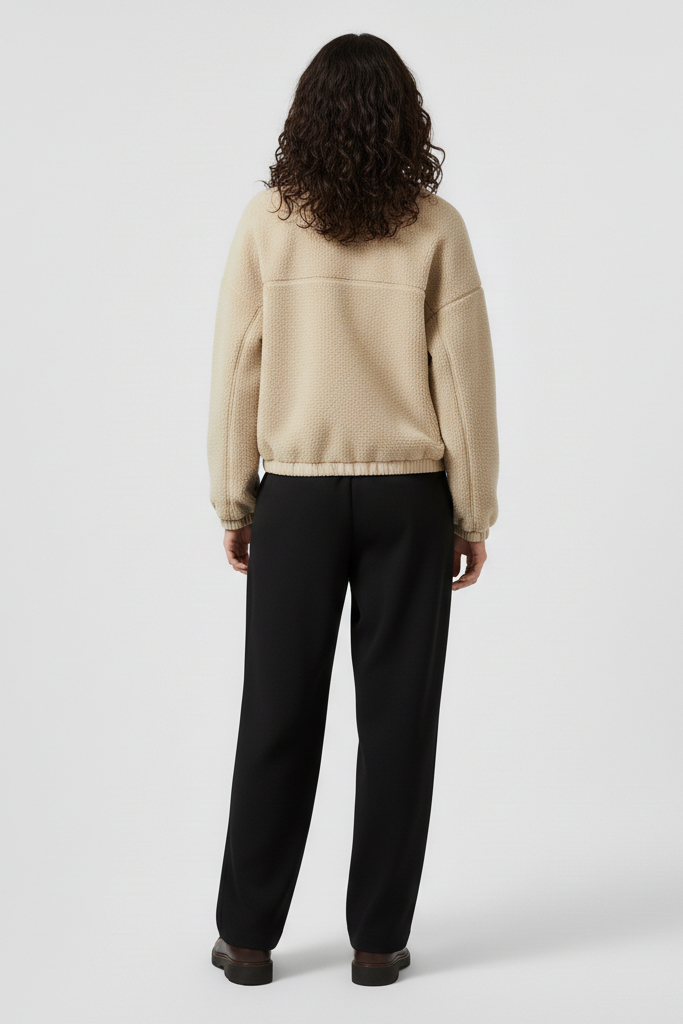 Person wearing a beige jacket and black pants on a white background