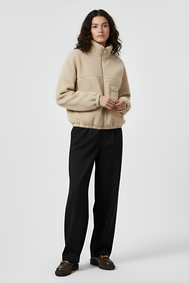 Person wearing a beige fleece jacket and black pants on a white background