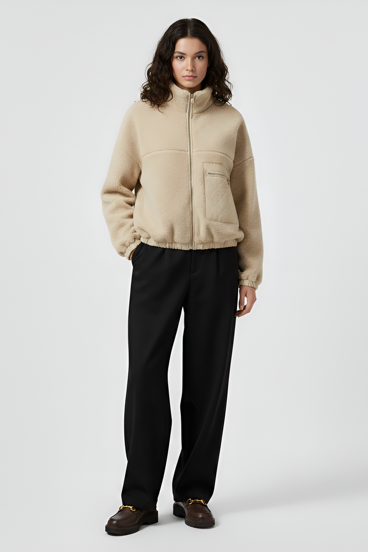 Person wearing a beige jacket and black pants on a white background