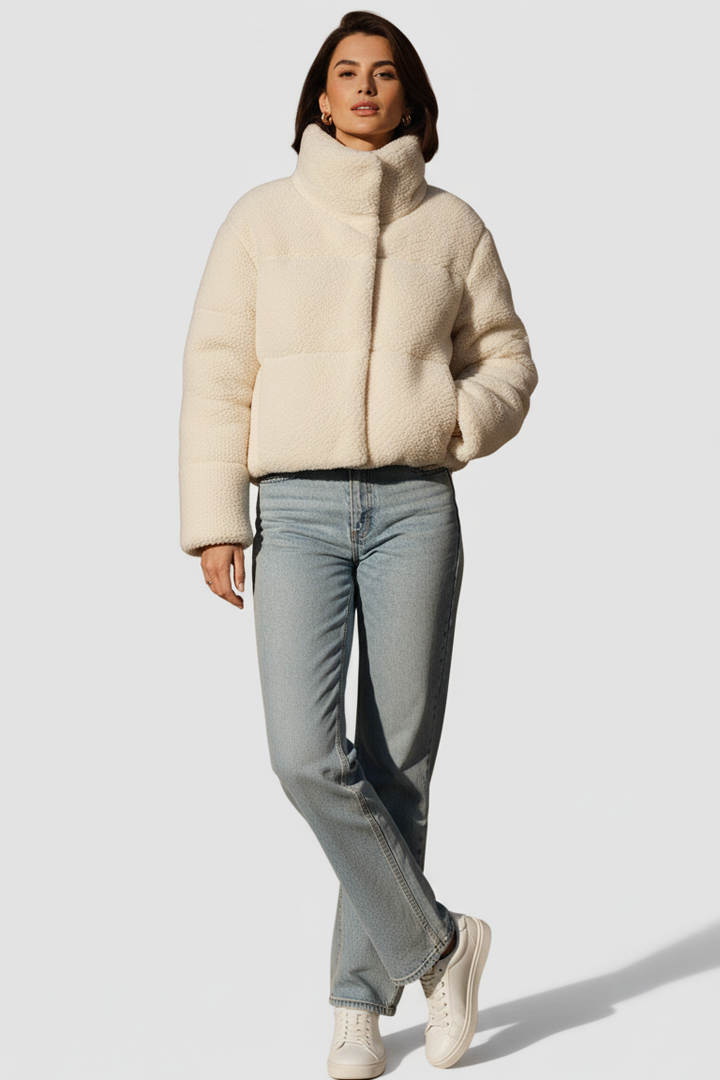 Person wearing a beige puffer jacket and light blue jeans on a white background