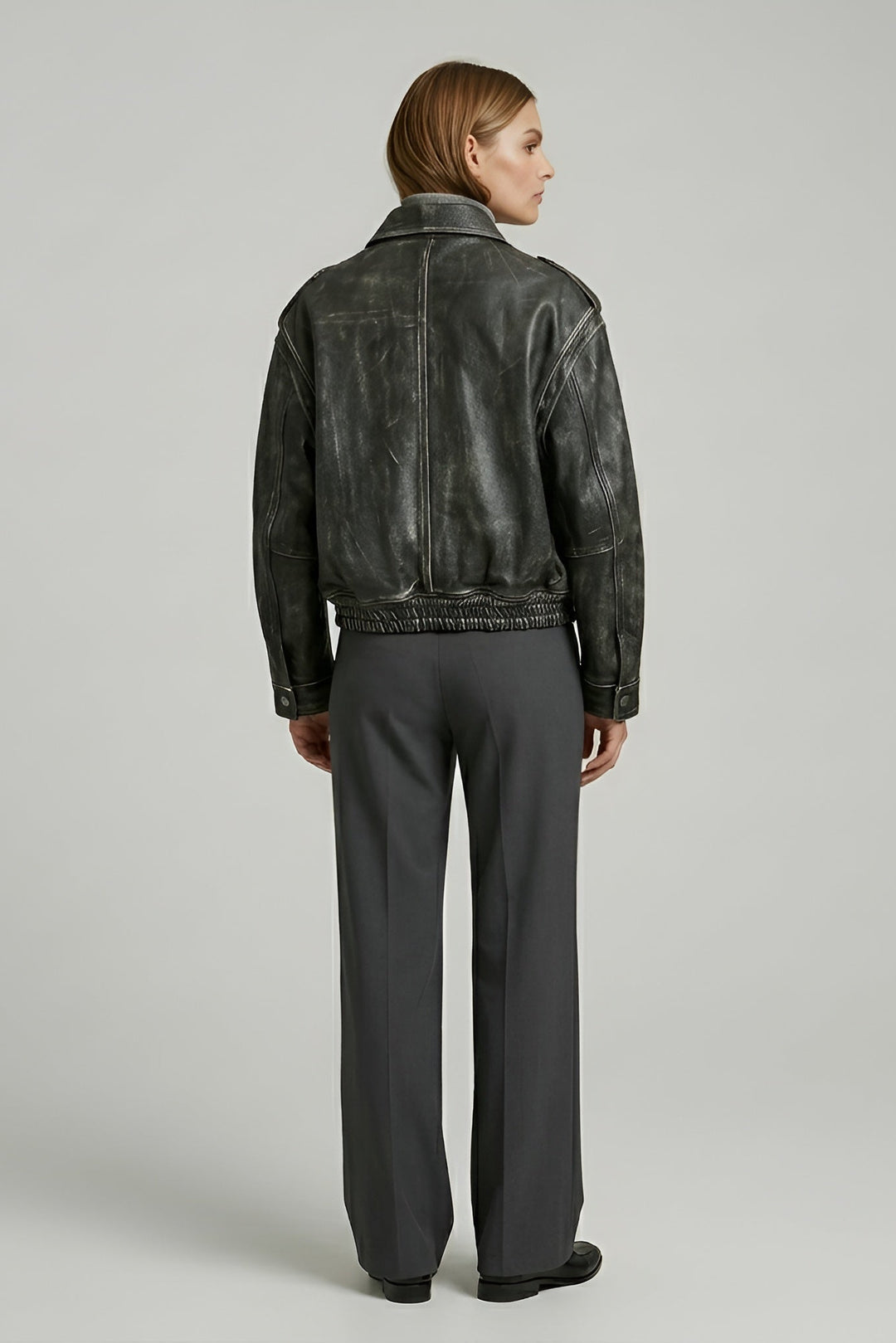 Person wearing a black leather jacket and gray pants on a light gray background