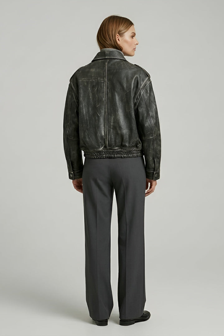 Person wearing a black leather jacket and gray pants on a light gray background
