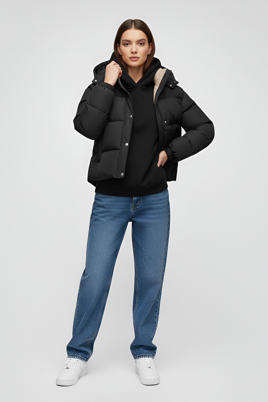 Person wearing a black puffer jacket and beige pants sitting on a white cube against a light gray background