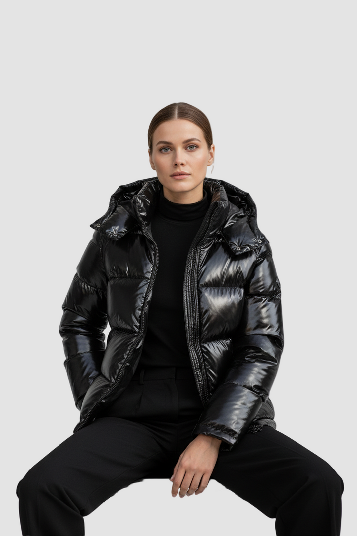 Person wearing a black puffer jacket sitting on a chair against a gray background