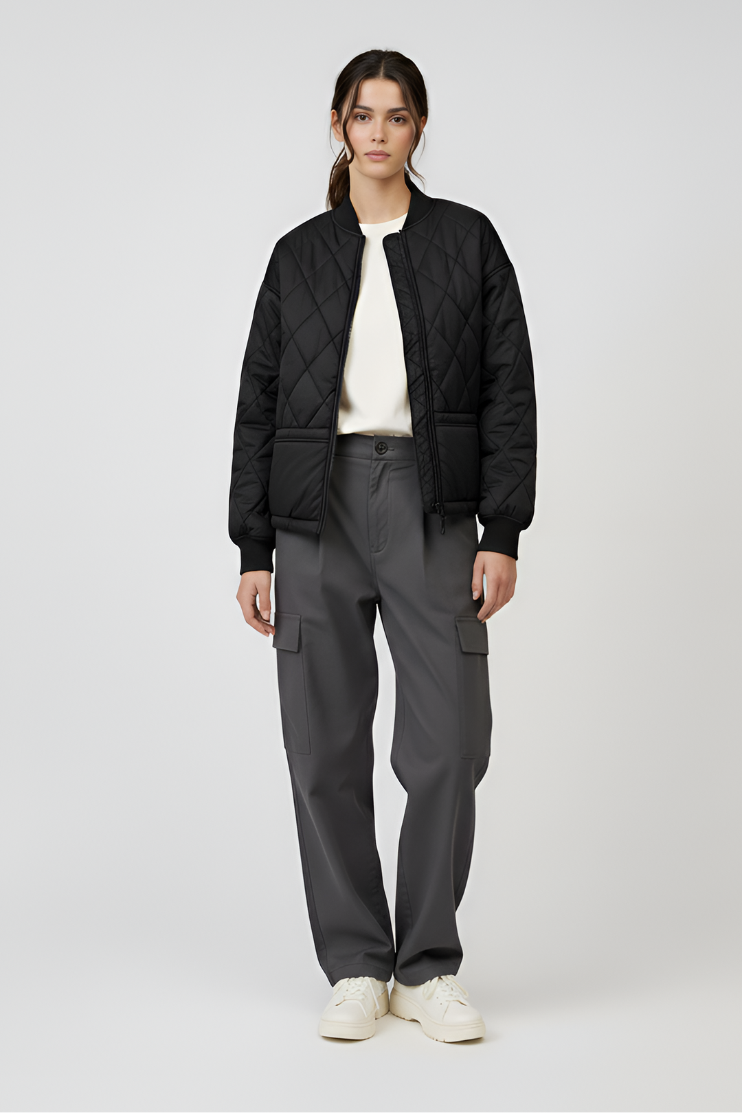 Person wearing a black quilted jacket and gray cargo pants on a white background