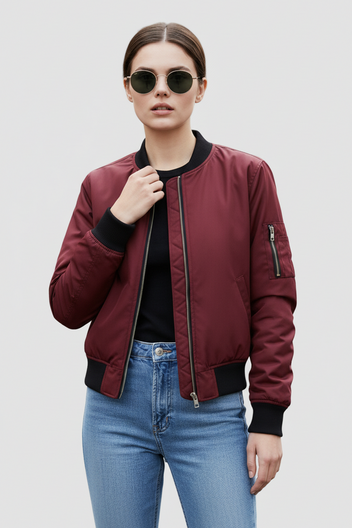 Person wearing a burgundy bomber jacket and blue jeans on a plain background