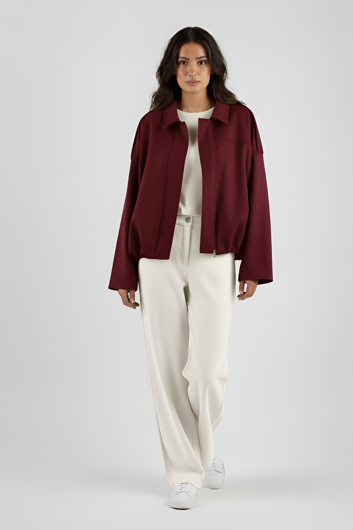 Person wearing a burgundy jacket and white pants on a plain background