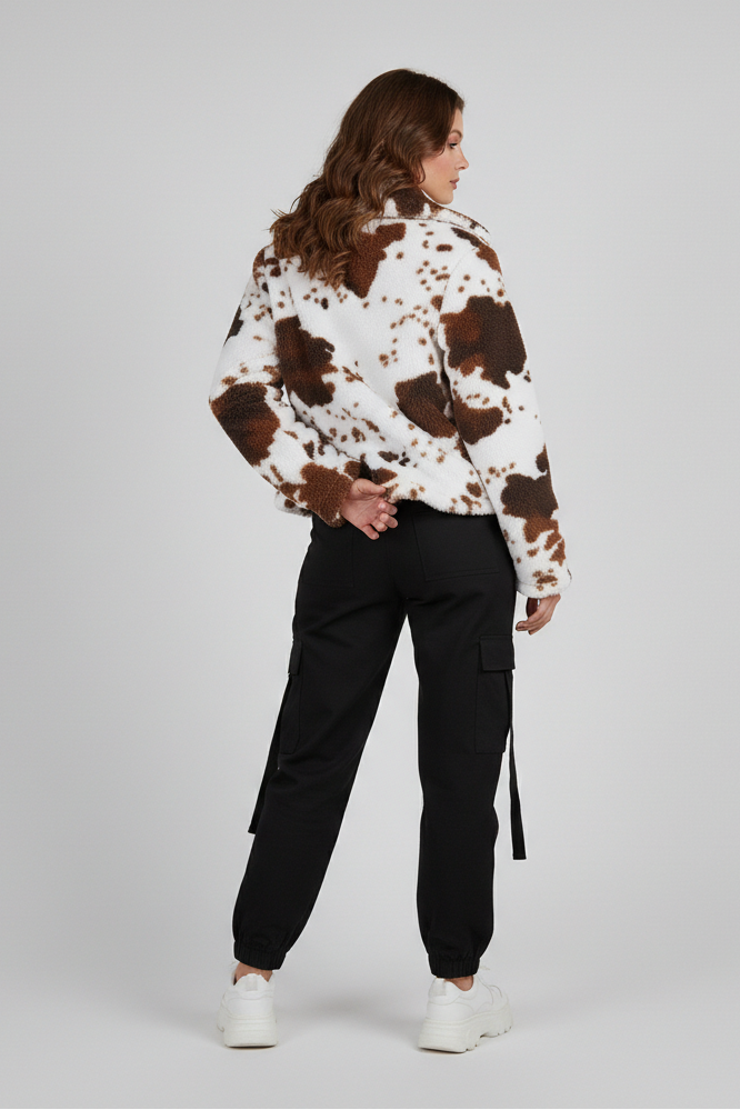 Person wearing a cow print jacket and black pants on a plain background