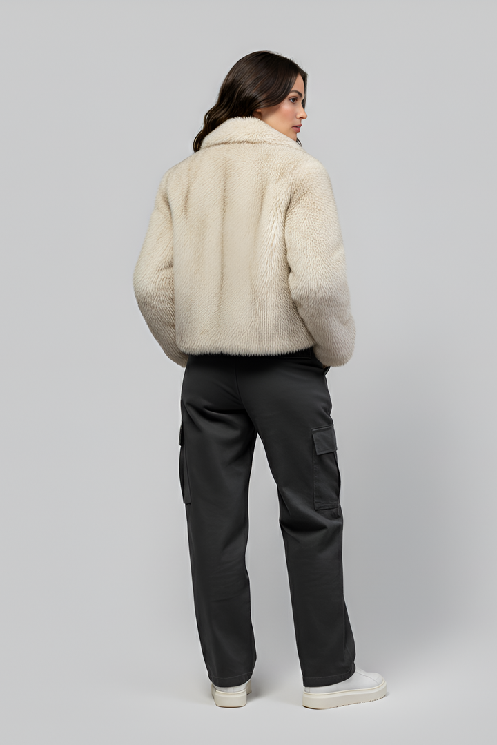 Person wearing a cream fur coat and dark pants on a light gray background