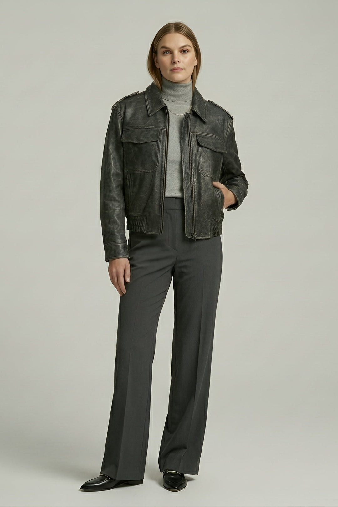 Person wearing a dark leather jacket and gray pants on a plain background