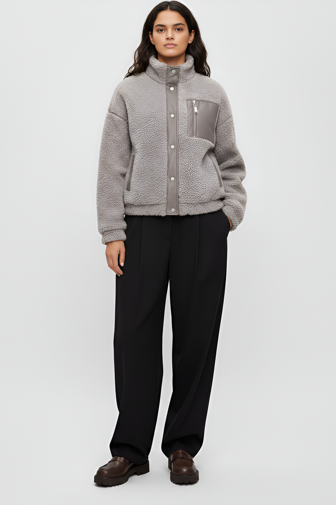 Person wearing a gray fleece jacket and black pants on a white background