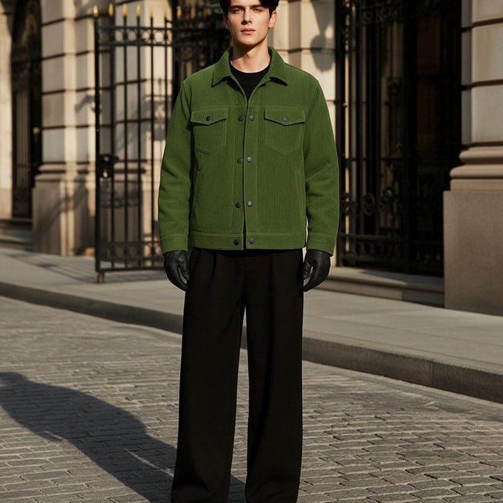 Person wearing a green jacket and black pants standing on a street.