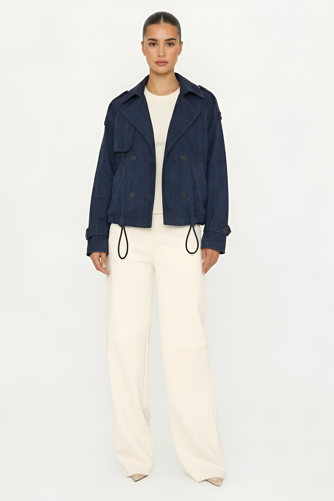 Person wearing a navy jacket and white pants on a white background