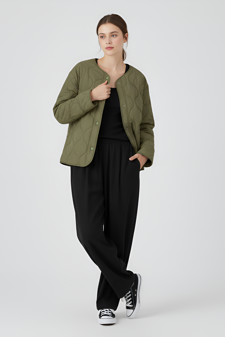 Person wearing a quilted green jacket, black leggings, and white sneakers on a gray background