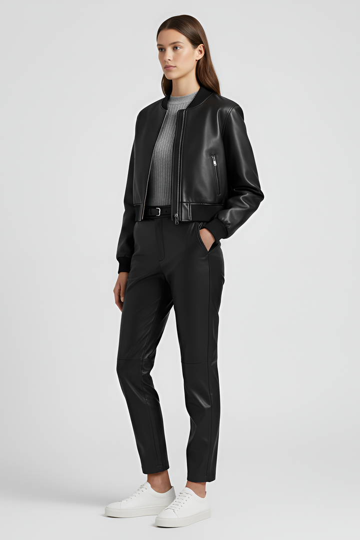 Person wearing a black leather bomber jacket and blue jeans on a white background