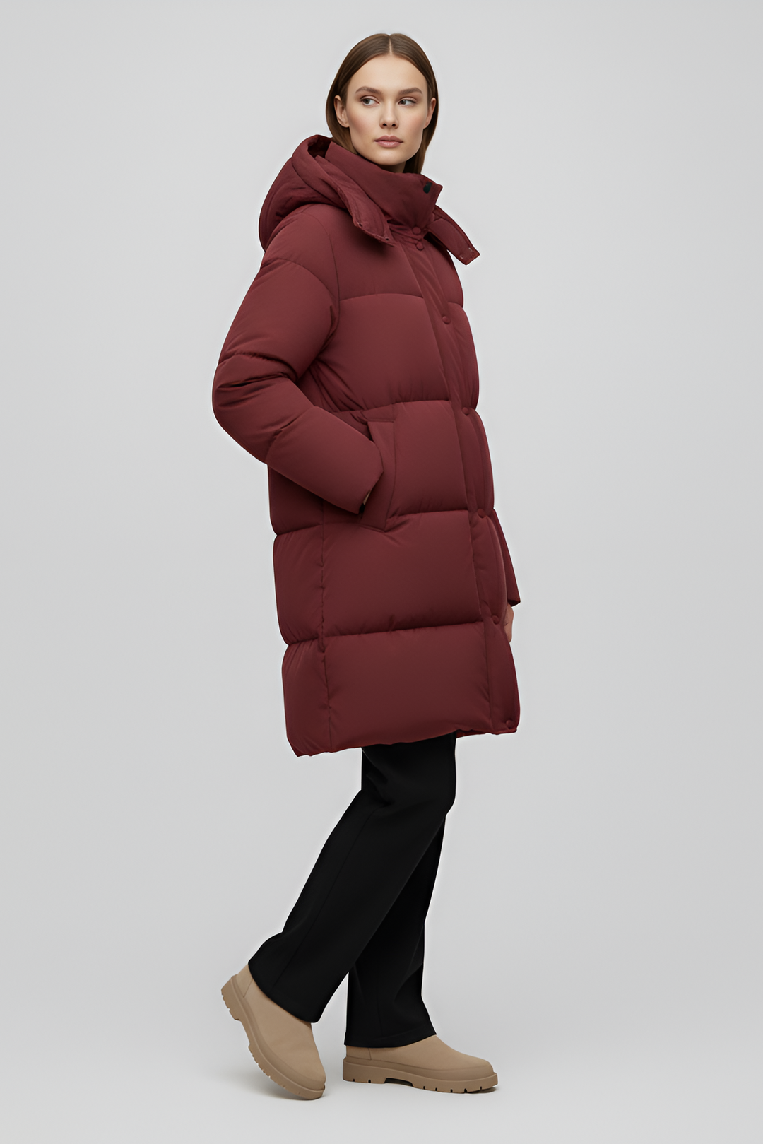 Person wearing a long burgundy puffer coat on a white background