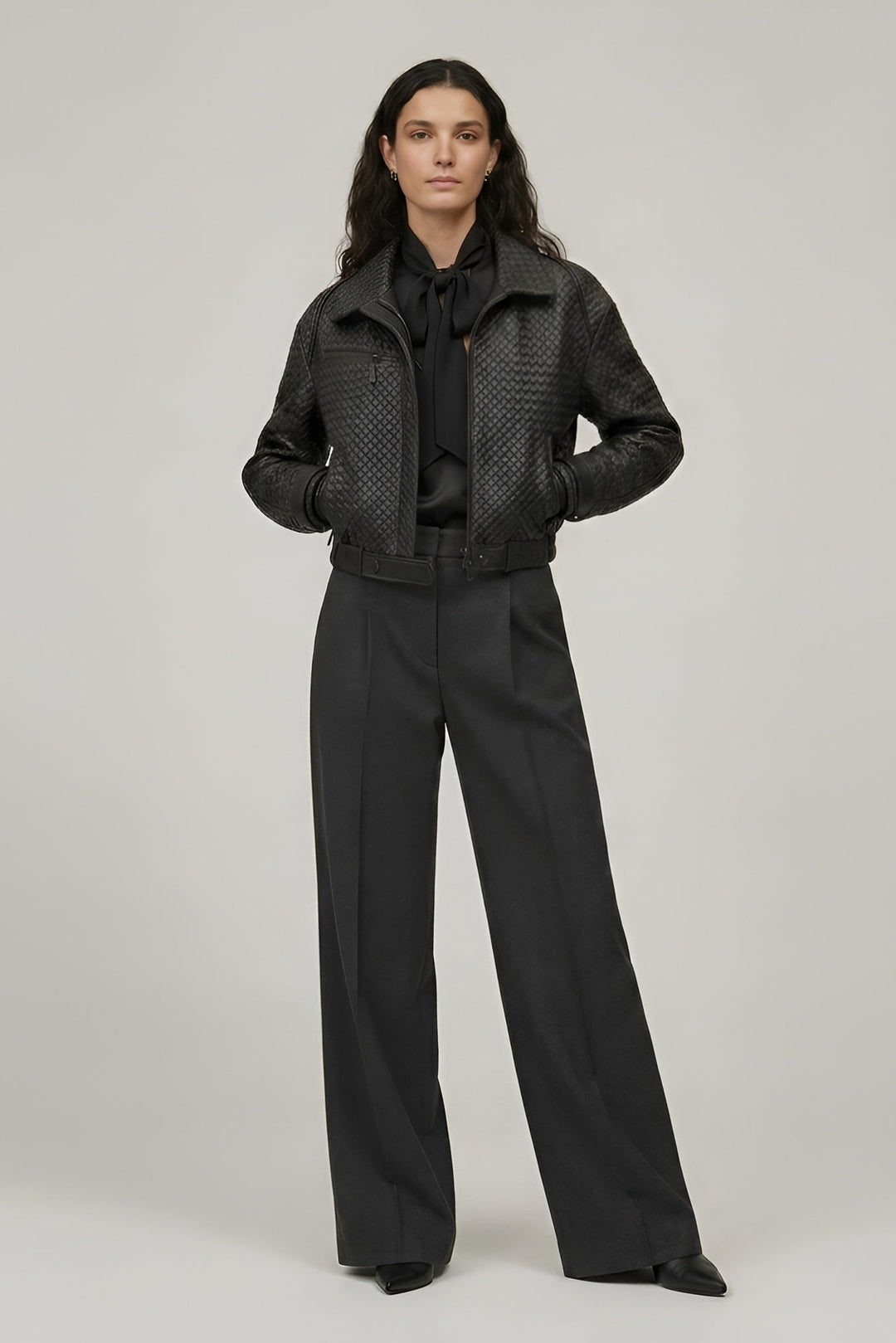 Woman wearing a black textured jacket and pants on a plain background