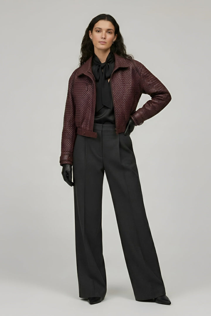 Woman wearing a burgundy leather jacket and black pants on a gray background