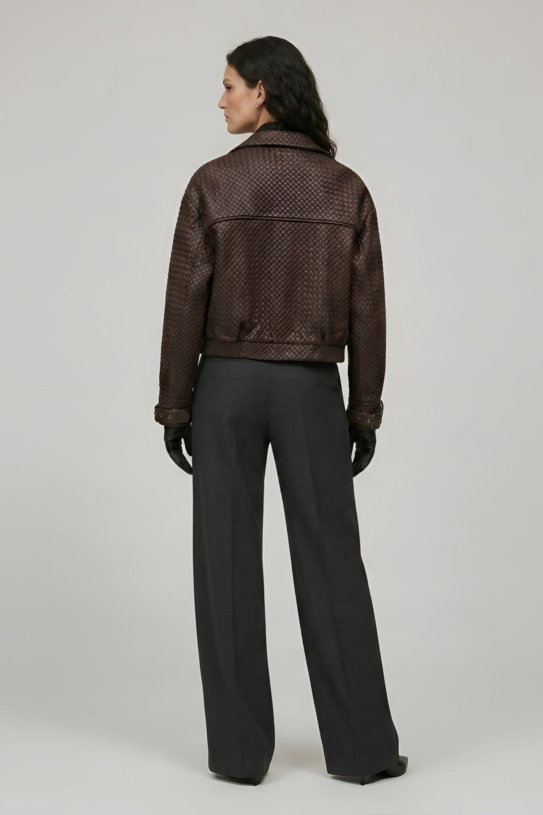 Person wearing a brown textured jacket and black pants on a plain background
