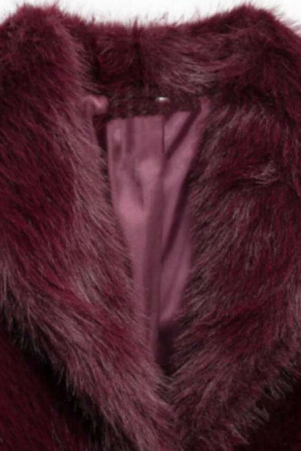 Stylish woman wearing the Camelia faux fur winter coat in deep burgundy, paired with black leather pants and boots for an elegant street look.