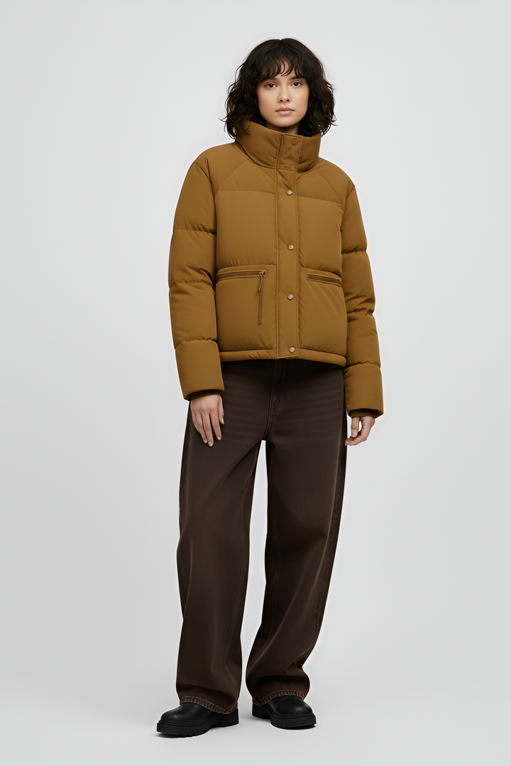 Woman wearing a Turmeric puffer jacket, brown sweater, black pants, and white shoes on a light gray background