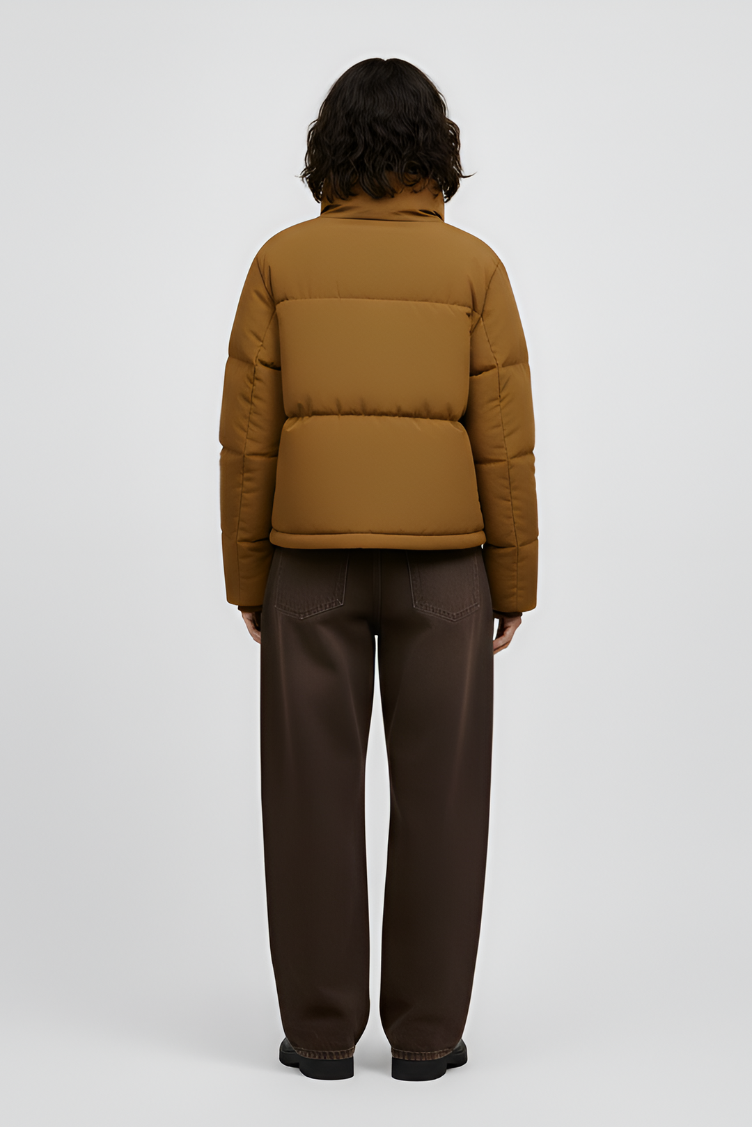 Woman wearing a Turmeric puffer jacket, brown sweater, black pants, and white shoes on a light gray background