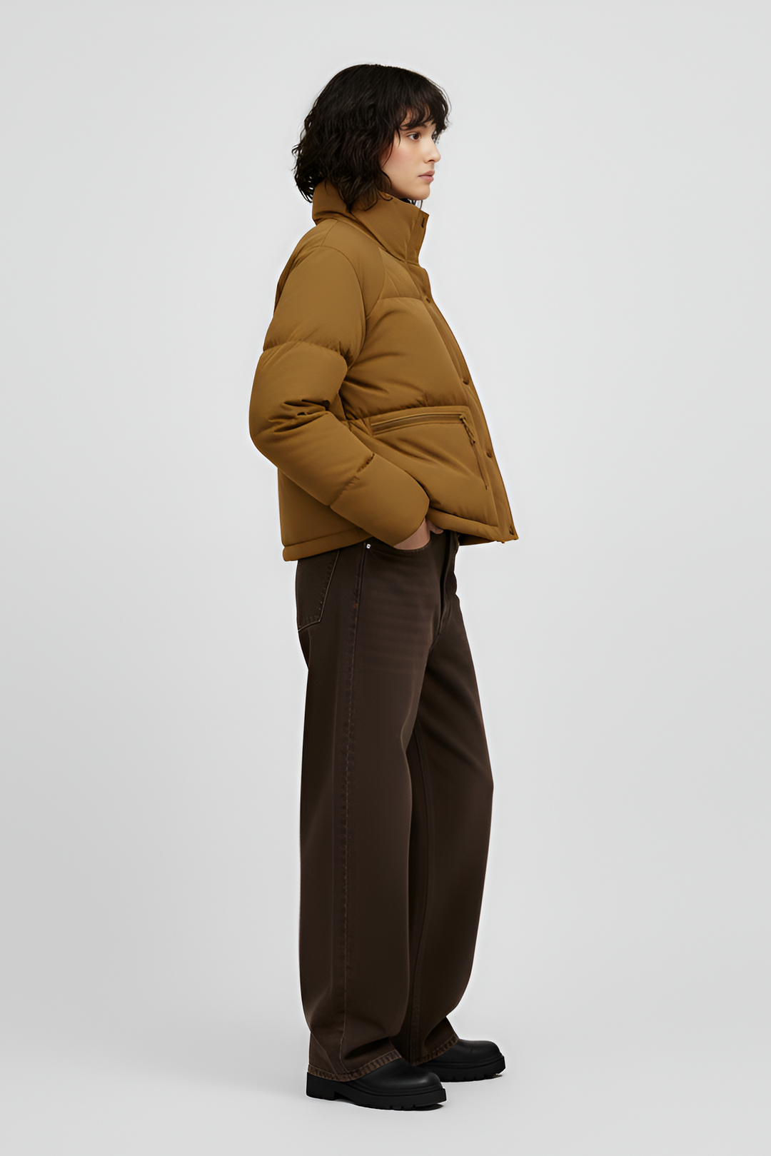 Woman wearing a Turmeric puffer jacket, brown sweater, black pants, and white shoes on a light gray background