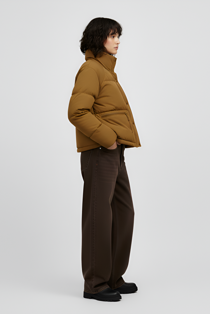 Woman wearing a Turmeric puffer jacket, brown sweater, black pants, and white shoes on a light gray background