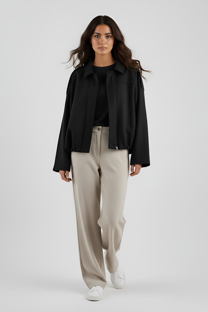 Woman wearing a black jacket and beige pants on a white background